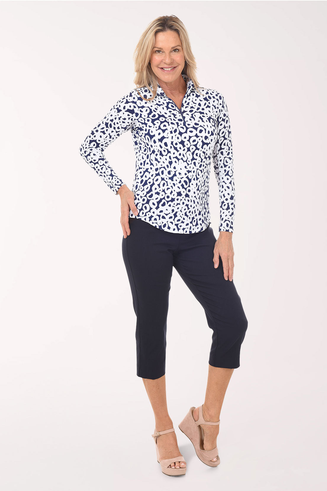 Woman wearing a patterned blouse and navy pants on a white background