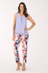 Woman wearing a light purple sleeveless top and colorful floral pants on a white background