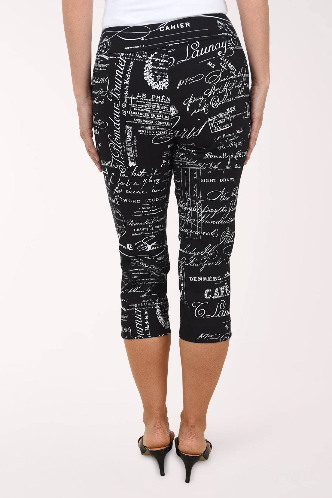 Black capri leggings with white text pattern worn by a person on a white background