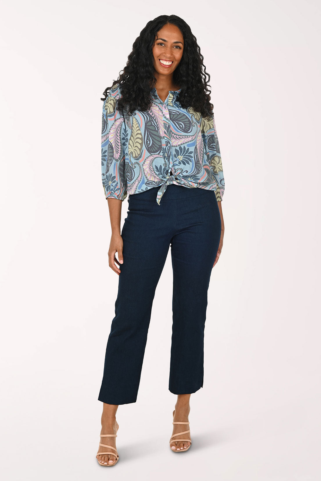 Woman wearing a patterned blouse and navy pants on a white background