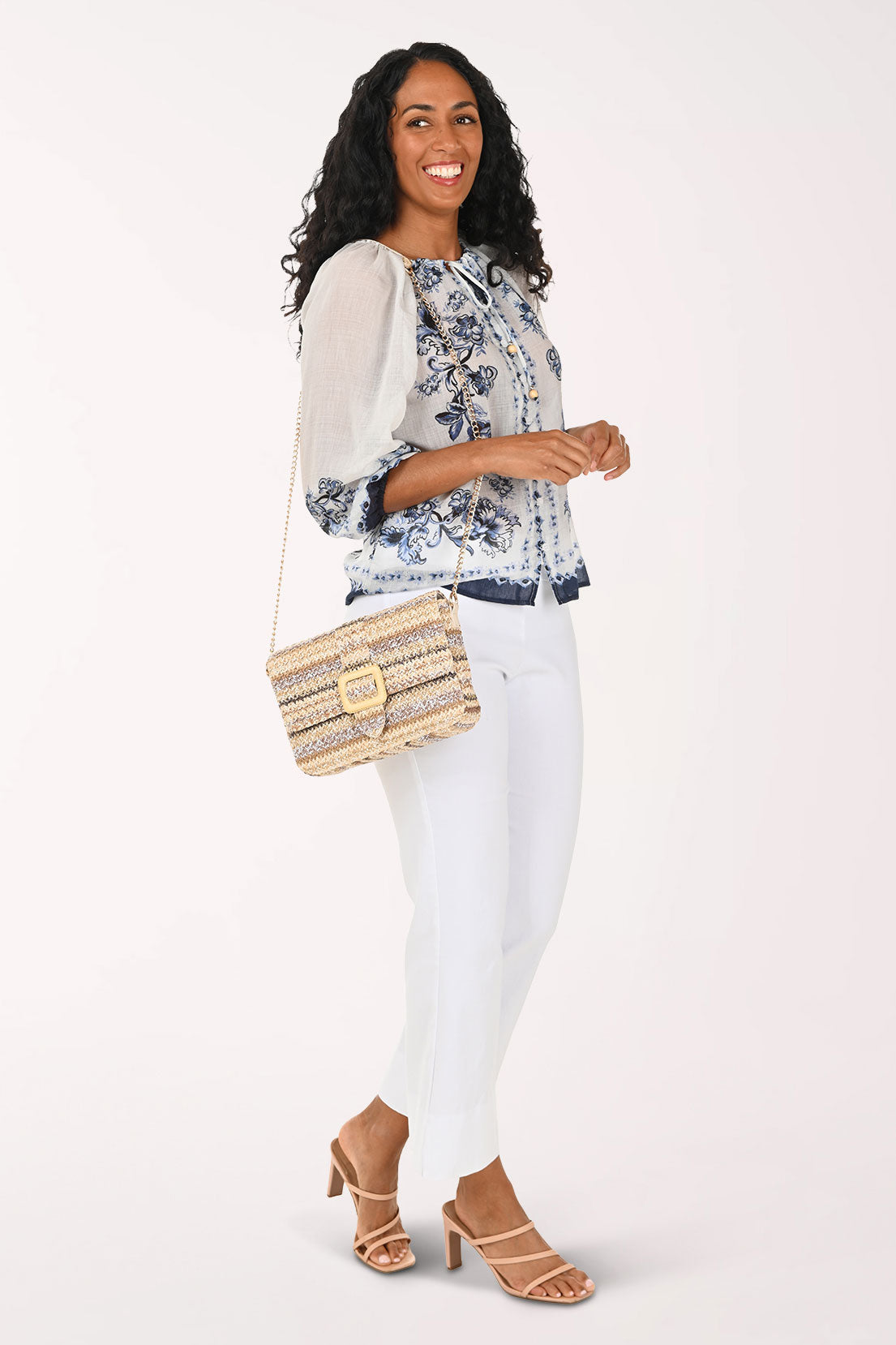 Woman wearing a floral blouse, white pants, and carrying a straw bag on a white background