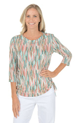 Woman wearing a patterned blouse with white pants on a white background.