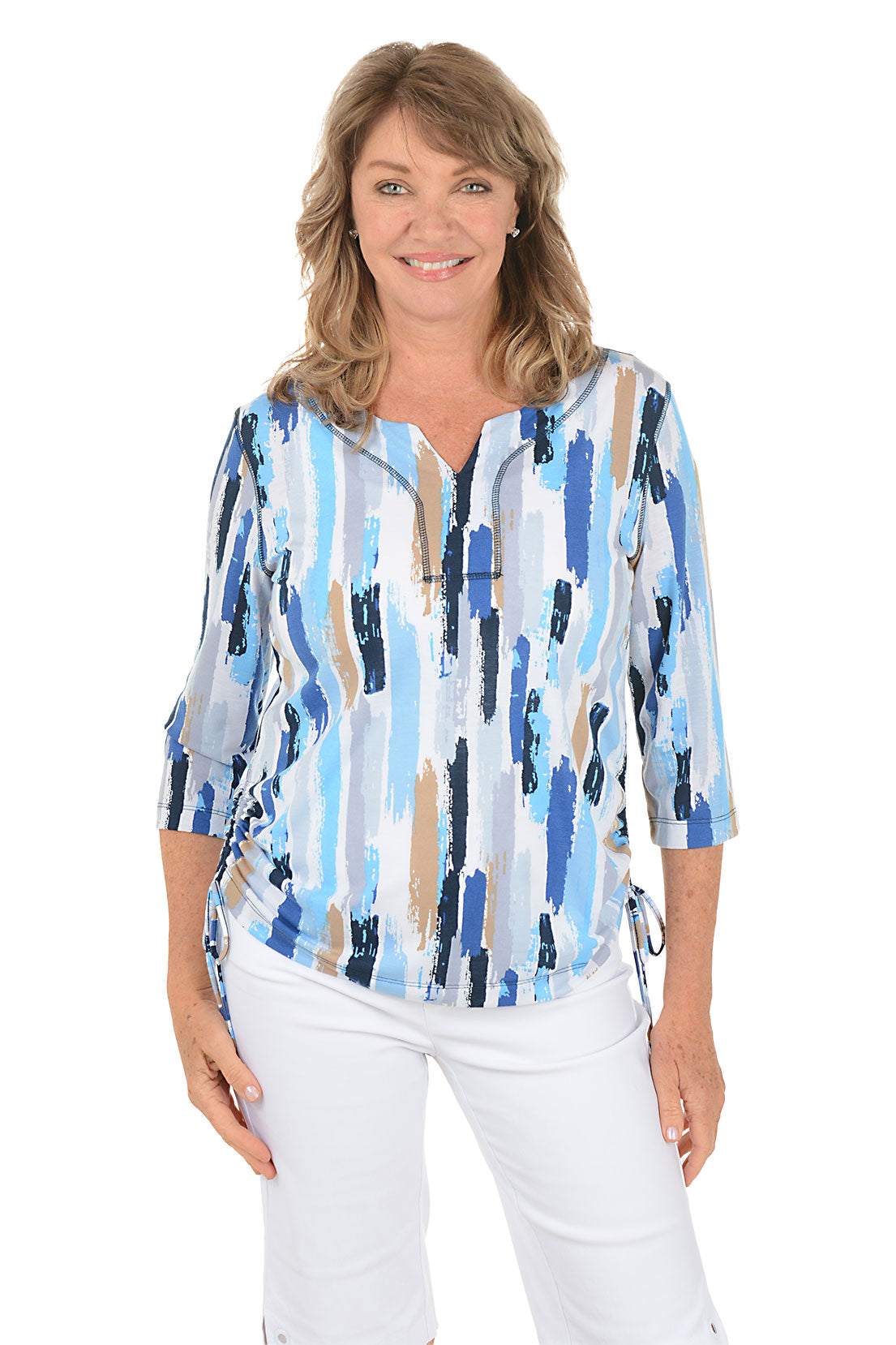 Woman wearing a blue and white patterned blouse with white pants on a white background.
