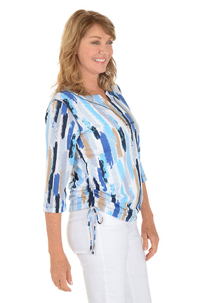 Woman wearing a blue and white patterned blouse with white pants on a white background. Side shot.