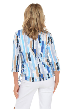 Woman wearing a blue and white patterned blouse with white pants on a white background. Back shot.