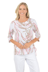 Woman wearing a white blouse with pink and gold abstract pattern on a white background.