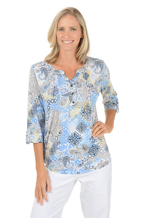 Woman wearing a patterned blouse with white pants on a white background.