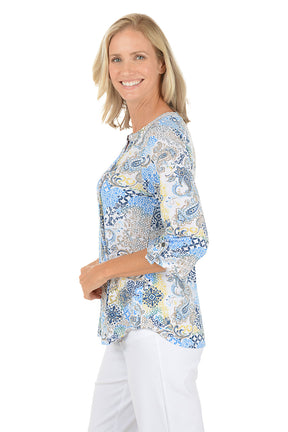 Woman wearing a patterned blouse with white pants on a white background. Side shot.