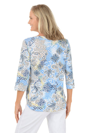 Woman wearing a patterned blouse with white pants on a white background. Back shot.