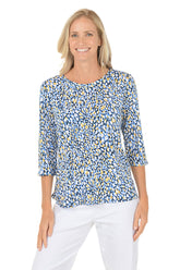 Woman wearing a blue and yellow patterned top with white pants on a white background.