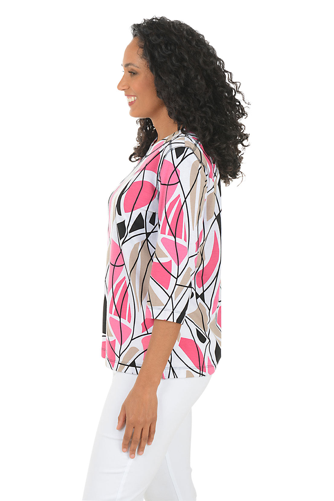 Woman wearing a colorful abstract patterned top and white pants on a white background. Side shot.