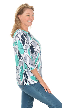 Woman wearing a blue colorful abstract patterned top and white pants on a white background. Side shot.