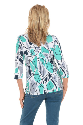 Woman wearing a blue colorful abstract patterned top and white pants on a white background. Back shot.