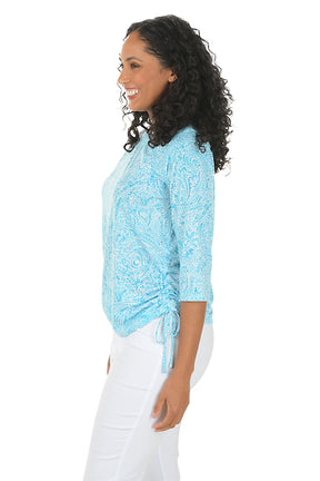 A woman wearing a 3/4 sleeve aqua top with ruched sides. Side shot.