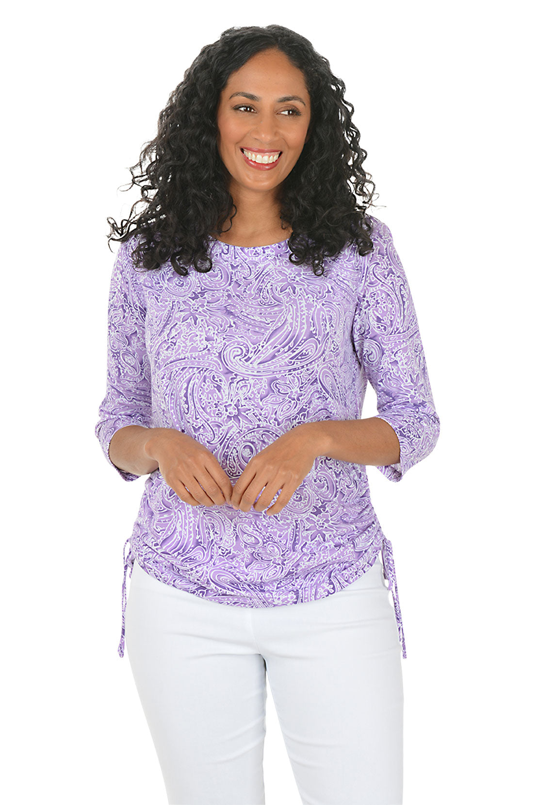 Woman wearing a purple paisley patterned top and white pants on a white background.
