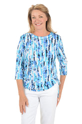 Woman wearing a blue tie-dye shirt with white pants on a white background.