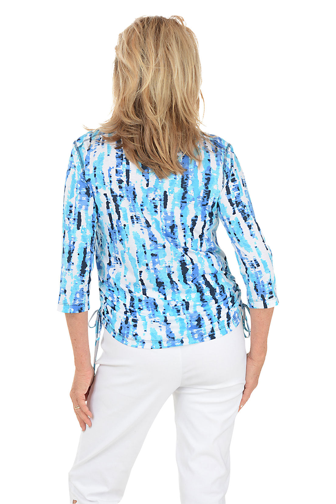 Woman wearing a blue tie-dye shirt with white pants on a white background. Back shot.