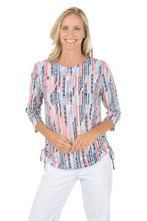 Woman wearing a colorful patterned top and white pants on a white background.