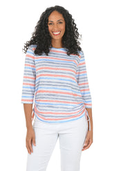 Woman wearing a colorful striped top and white pants on a white background.