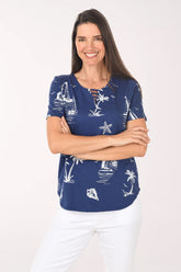 Woman wearing a blue patterned top with white pants on a white background