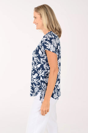 Woman wearing a short sleeve blue shirt with shell and coral details