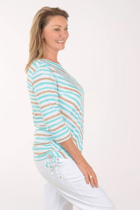 Woman wearing a striped turquoise and beige top with white pants on a white background