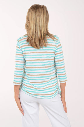 Woman wearing a striped turquoise and beige top with white pants on a white background