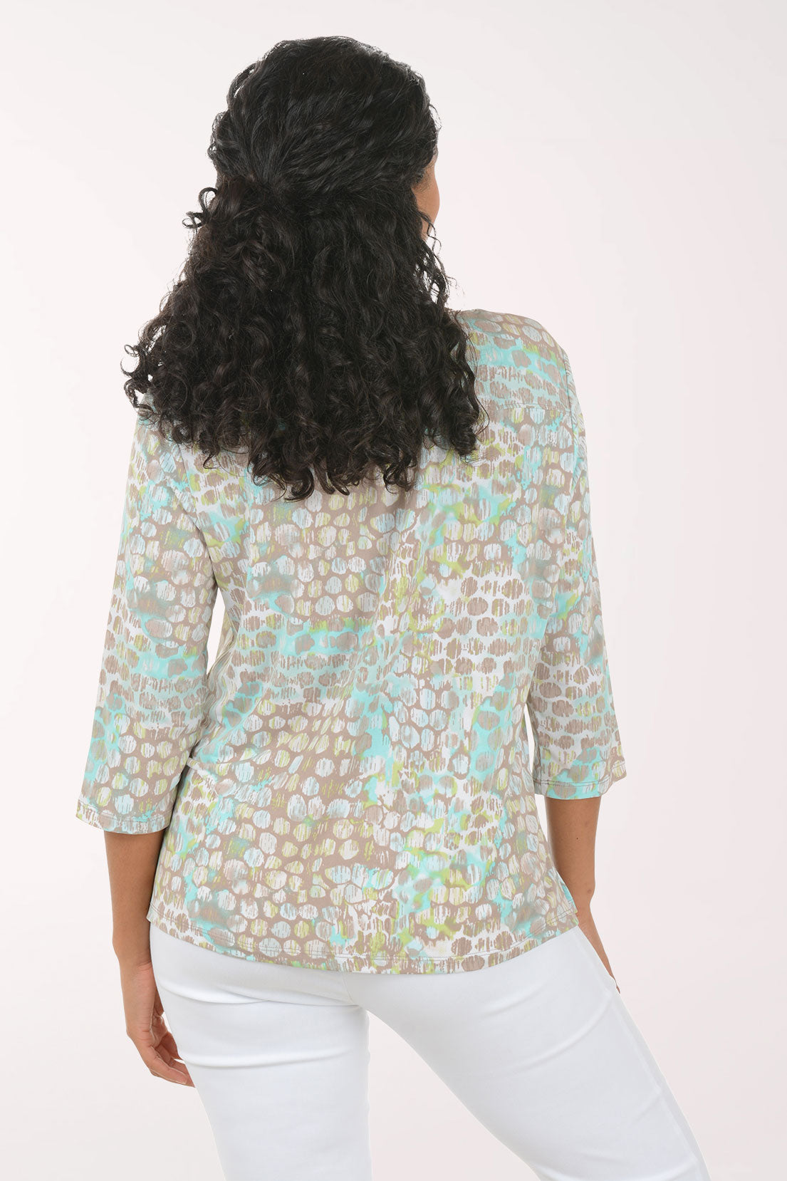 Woman wearing a floral blouse with white pants on a plain background