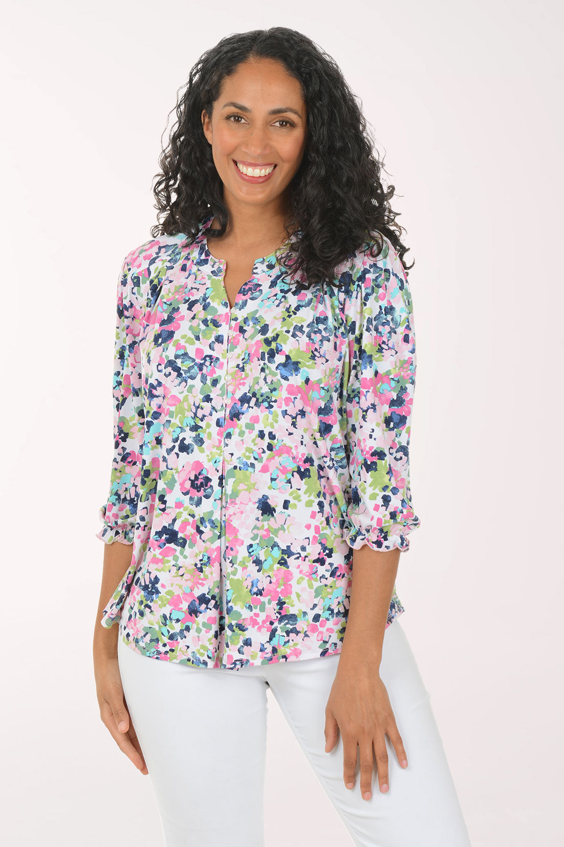 Woman wearing a floral blouse and white pants on a light pink background