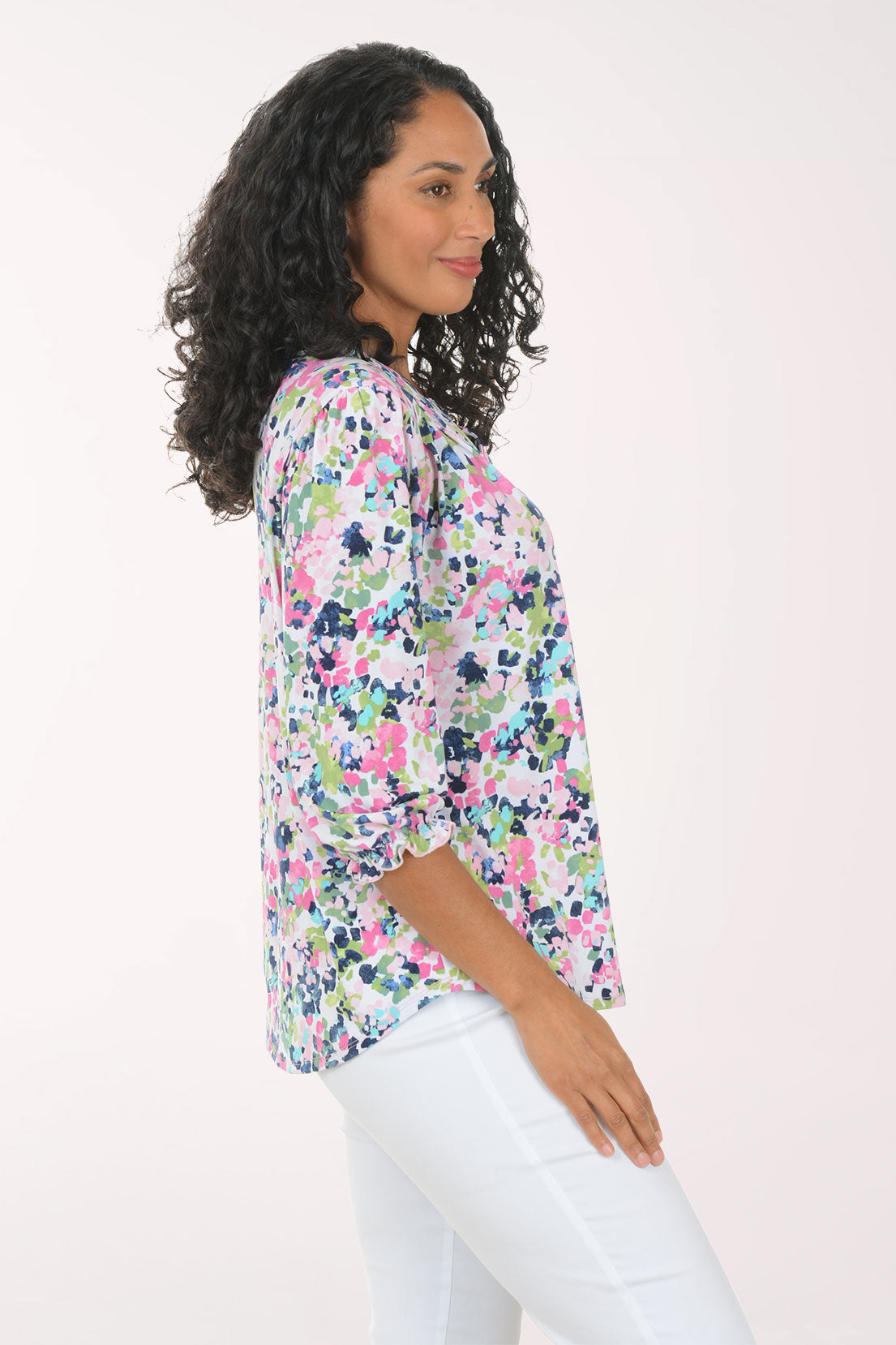 Woman wearing a floral blouse and white pants on a light pink background