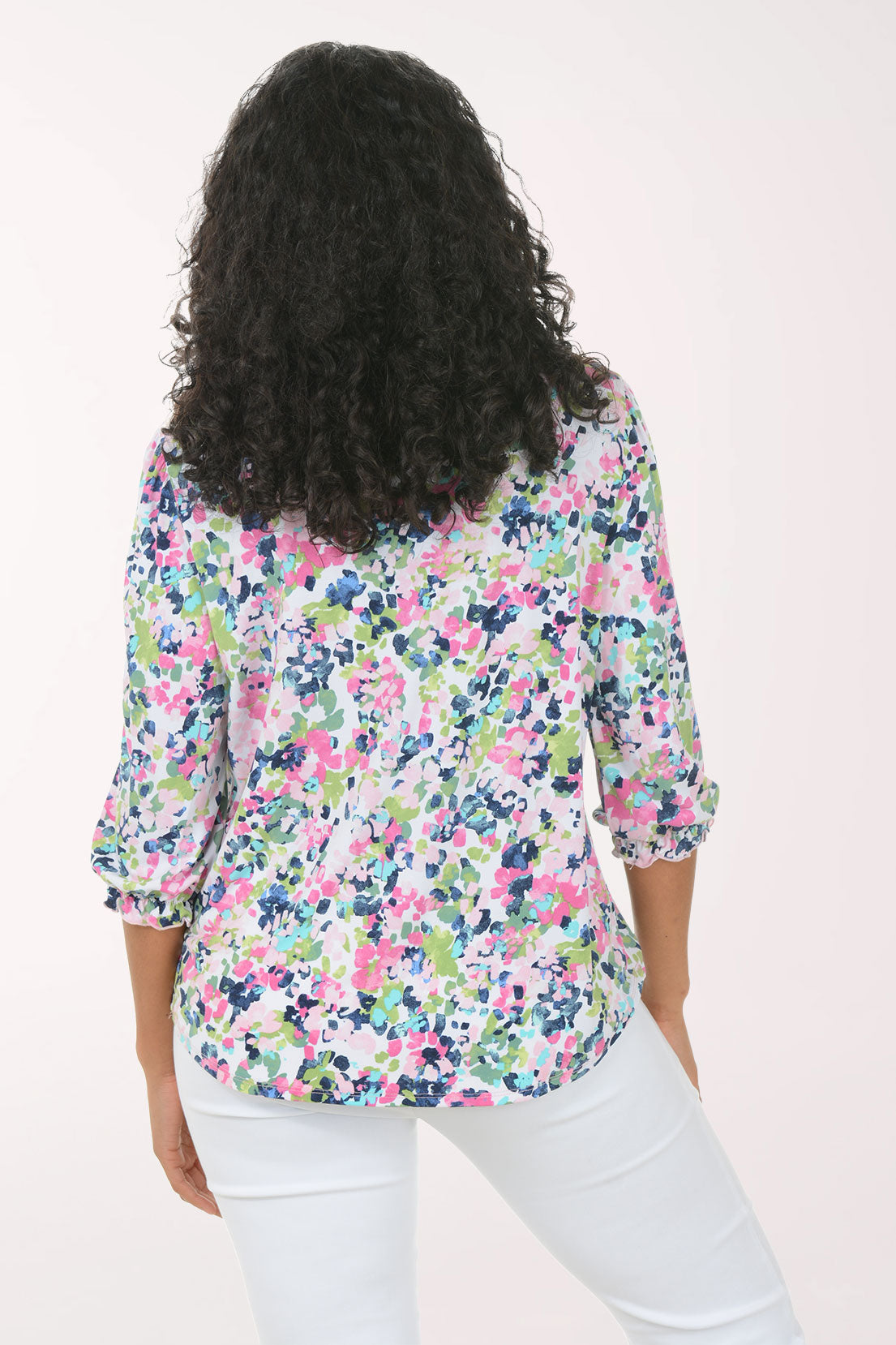 Woman wearing a floral blouse and white pants on a light pink background