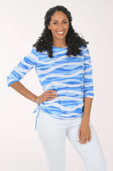 Woman wearing a blue and white patterned top with white pants on a white background