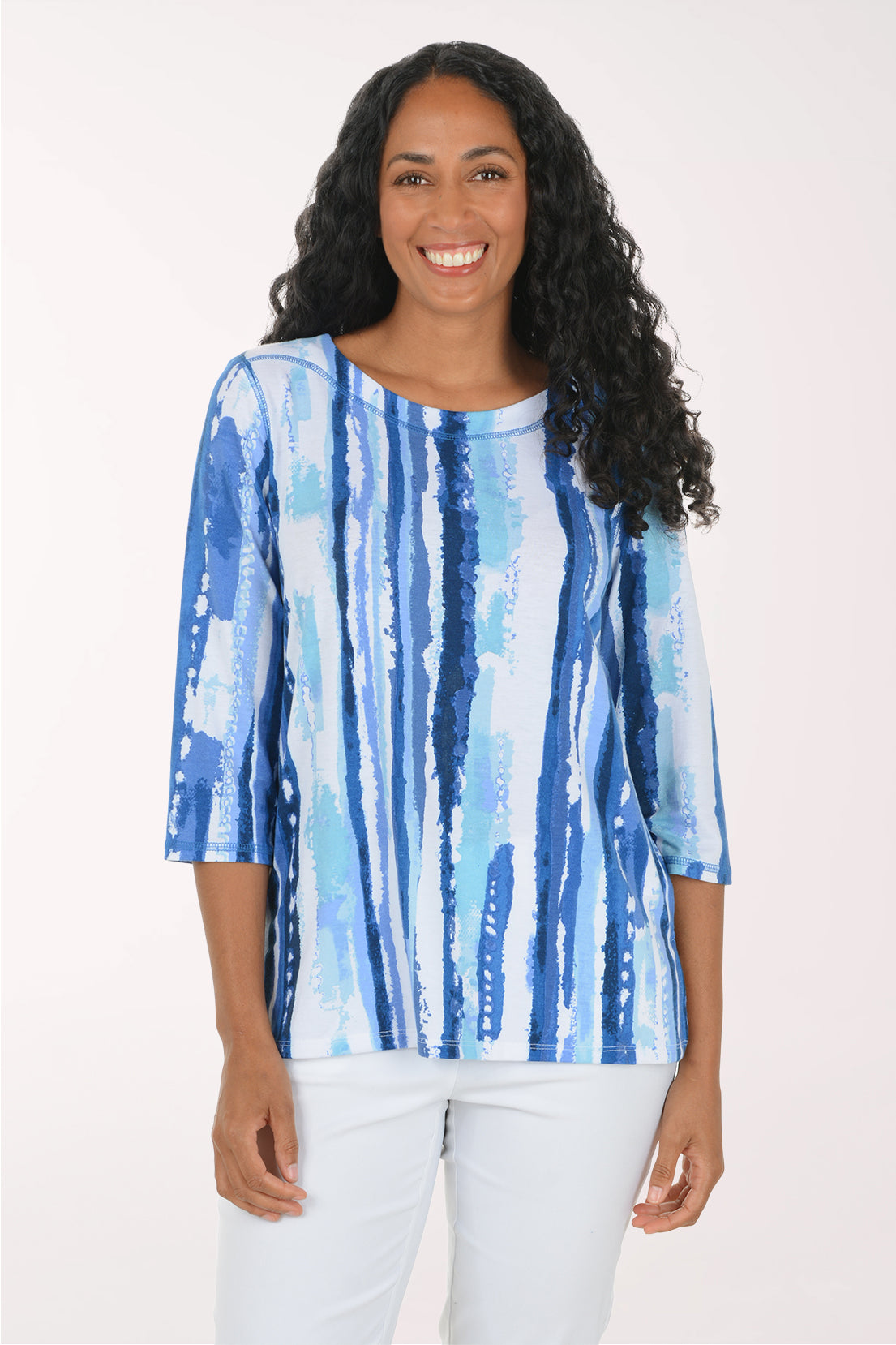 A woman modeling a blue and white vertically striped top with three-quarter sleeves, paired with white pants, against a plain white studio background.