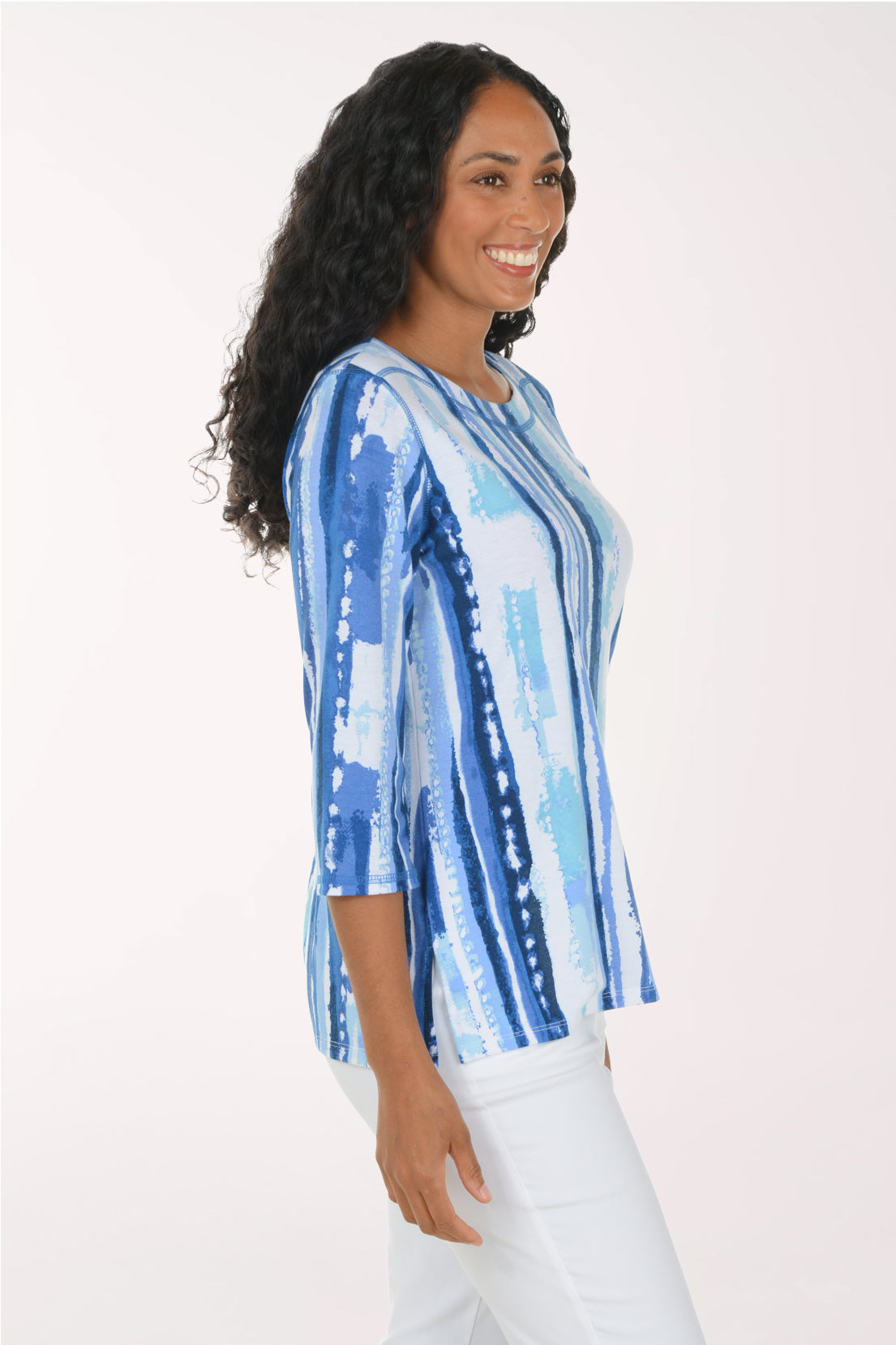 A woman modeling a blue and white vertically striped top with three-quarter sleeves, paired with white pants, against a plain white studio background.