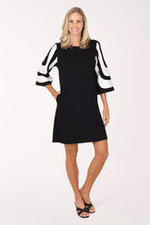 Front view of a model wearing the Lior Monochrome Mod Color Block Dress, a black above-the-knee shift dress with flared 3/4 sleeves in a curved black and white color block design, worn with black heeled sandals.
