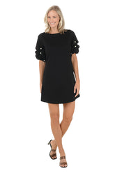 Woman wearing a black dress with pearl embellishments on a white background.