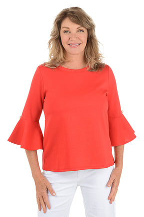 Woman wearing a red bell-sleeve top and white pants on a white background.