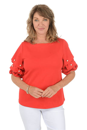 Woman wearing a red blouse with pearl embellishments on a white background
