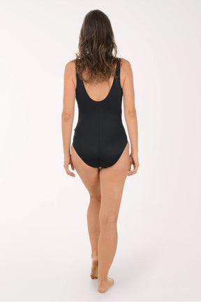 Woman wearing a blue and black patterned swimsuit on a white background. Back shot.