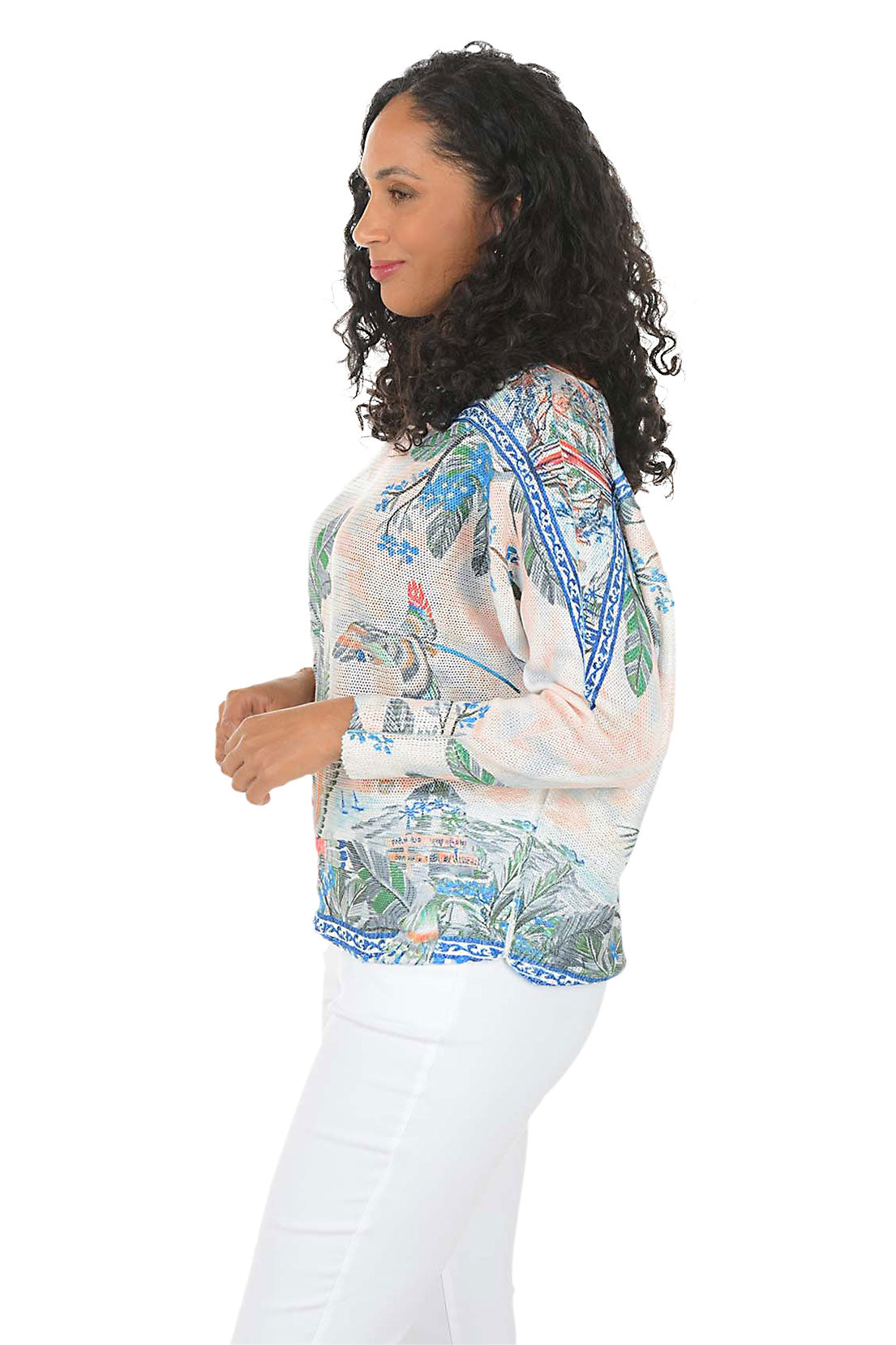 Woman wearing a tropical patterned blouse with palm trees and flowers on a white background. Side shot.