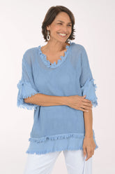Woman wearing a light blue textured top with ruffled edges on a white background