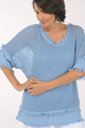Woman wearing a light blue textured top with ruffled edges on a white background