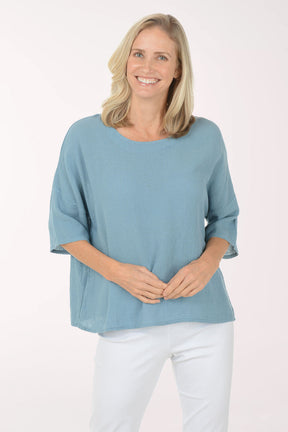 Woman wearing a blue top and white pants on a white background