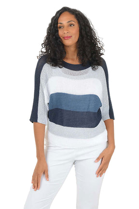 Woman wearing a blue and white patterned top with white pants on a white background.