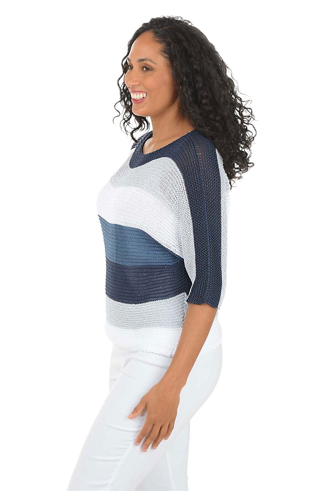 Woman wearing a blue and white patterned top with white pants on a white background. Side shot.