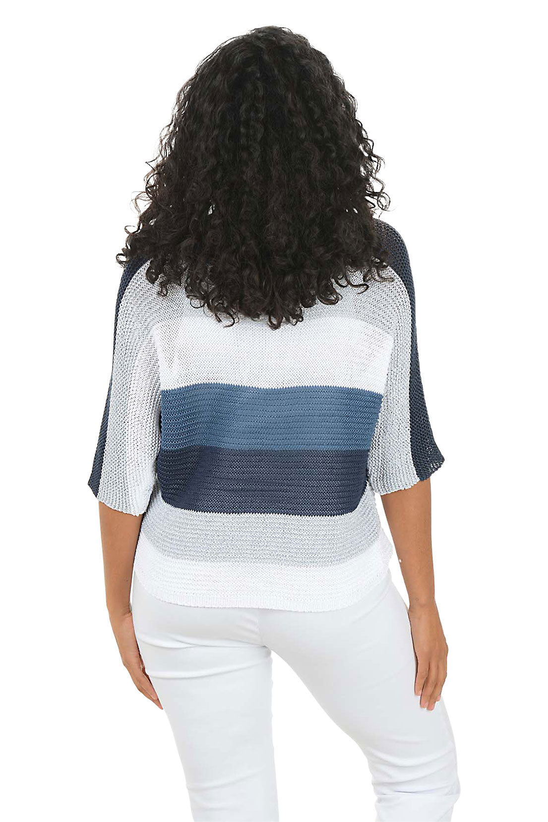 Woman wearing a blue and white patterned top with white pants on a white background. Back shot.