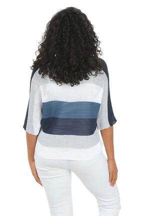 Woman wearing a blue and white patterned top with white pants on a white background. Back shot.