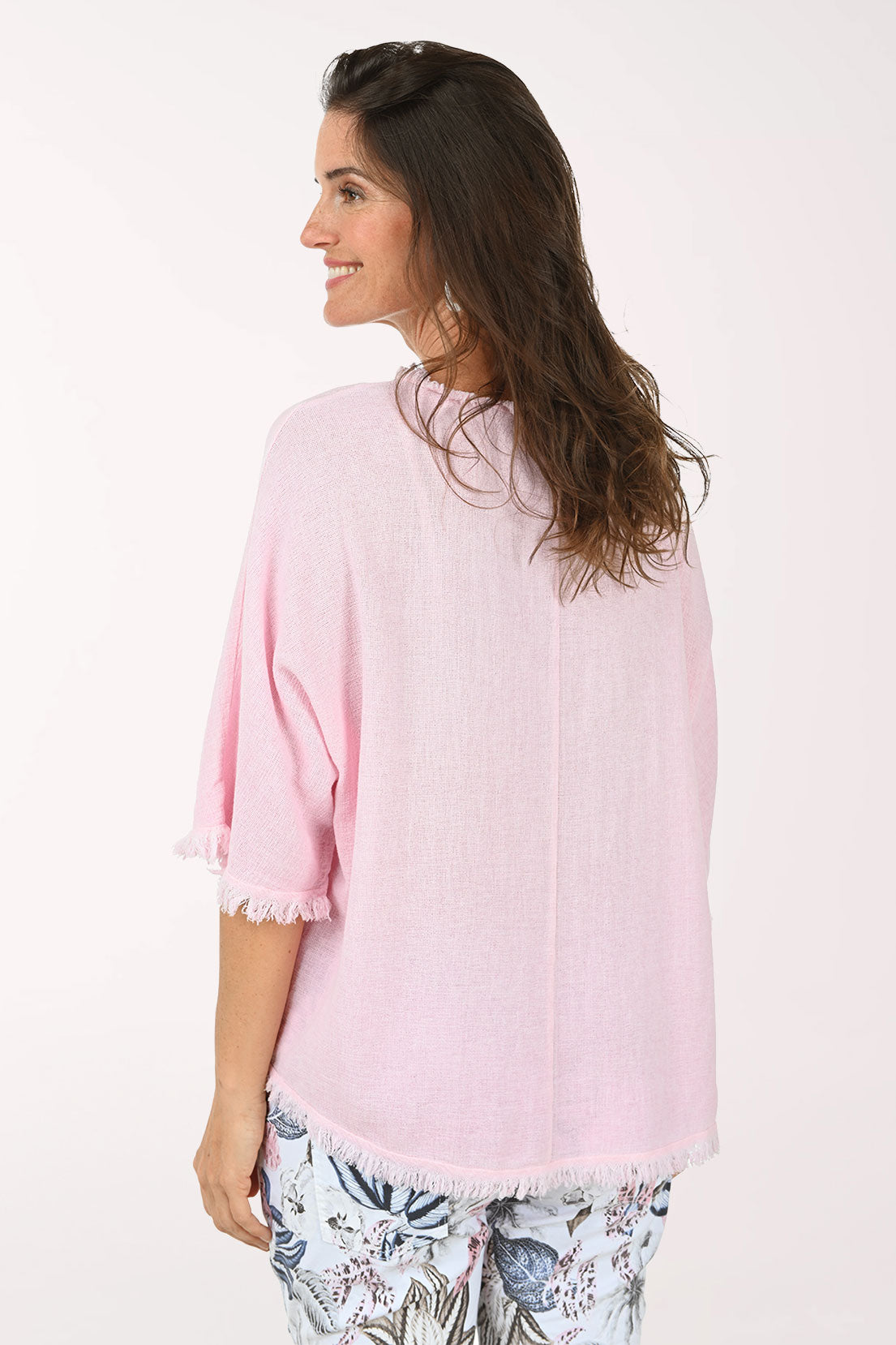 Woman wearing a light pink blouse with fringe details on a white background