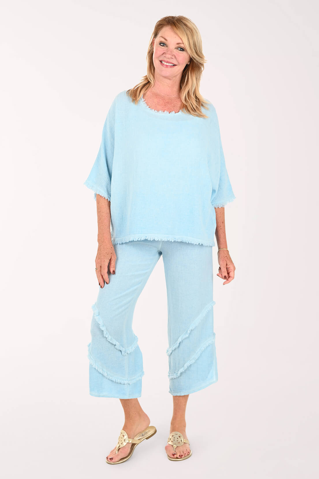 A woman modeling a light blue two-piece lounge set consisting of a short-sleeve top and matching cropped pants with ruffle trim, against a plain light background.