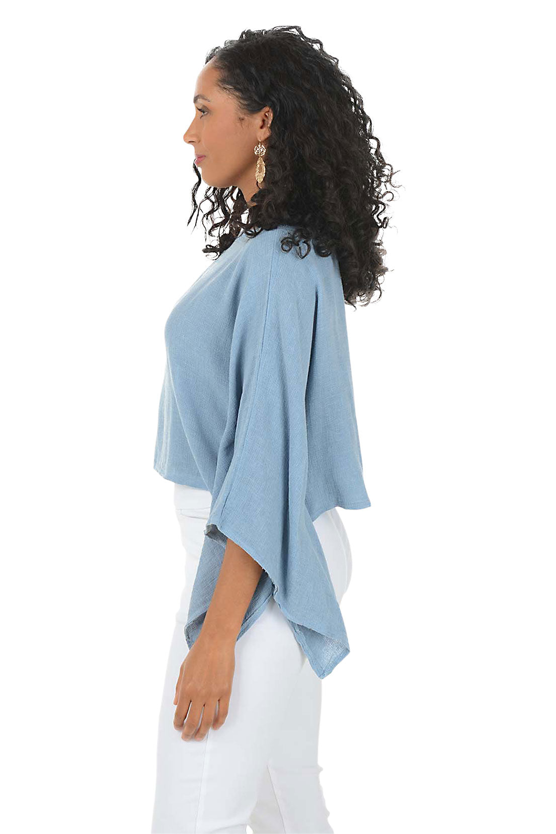 Woman wearing a blue sweater and white pants on a white background. Side shot.